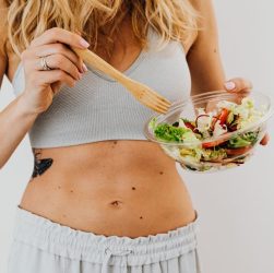 Young woman in sports attire holding a fresh salad bowl, promoting a healthy lifestyle.